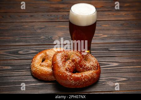 Leckere frisch gebackene Brezeln und ein Glas Bier auf einem Holztisch Stockfoto