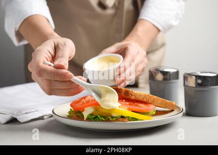 Eine Frau macht Sandwich mit Mayonnaise am grauen Tisch, Nahaufnahme Stockfoto