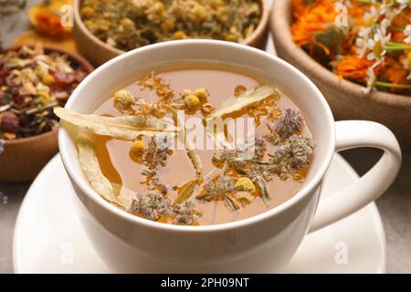 Tasse aromatischer, frisch gebrühter Tee und verschiedene trockene Kräuter auf dem Tisch, Nahaufnahme Stockfoto