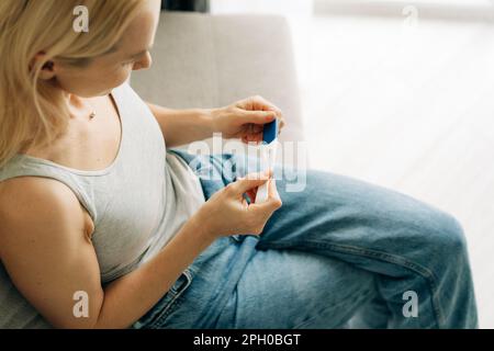 Eine Frau hält einen Schwangerschaftstest in den Händen und wartet auf das Ergebnis, wenn sie auf der Couch sitzt. Stockfoto