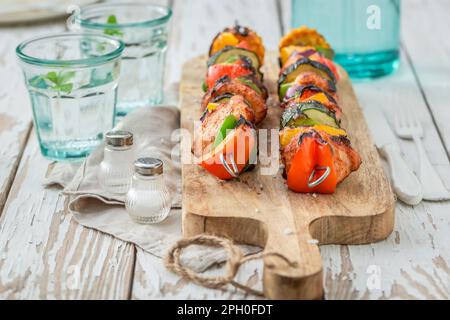 Hausgemachte und köstliche gegrillte Spieße serviert mit Zitruswasser im Garten. Grillspieße auf dem Grill mit Fleisch und Gemüse. Stockfoto