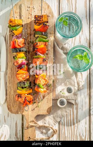 Leckere und heiße Grillspieße serviert mit Zitruswasser im Garten. Grillspieße auf dem Grill mit Fleisch und Gemüse. Stockfoto