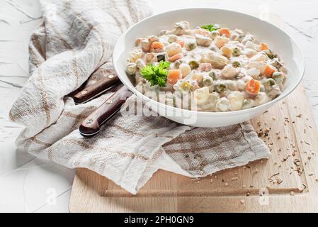 Schale mit russischem Salat olivier französischer Salat mit Gemüse und Ei mit Mayonnaise auf weißem Tisch Stockfoto