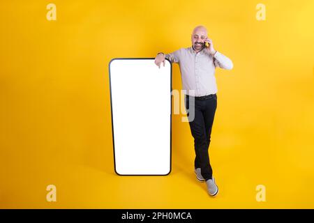 Ein weißer Mann mittleren Alters lehnt sich an ein großes Smartphone mit leerem weißen Bildschirm für ein Modell. Am Telefon. Speicherplatz kopieren. Stockfoto