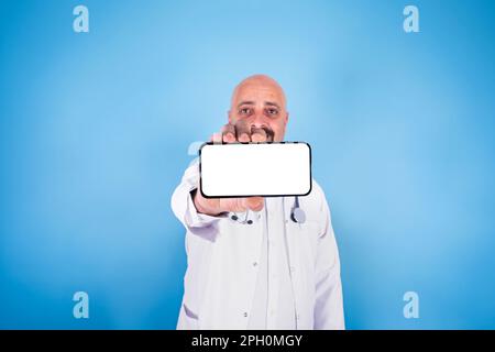 Arzt zeigt Smartphone, weißer Arzt mittleren Alters zeigt Smartphone. E-Verschreibung, Apotheke, Check-up, Konzeptidee zur Behandlung online. Modell. Stockfoto