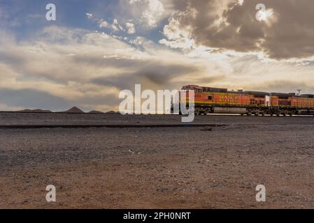 Ein leuchtend orangefarbener BNSF Railway-Güterzug fährt durch die kalte Wüste von Yeso, New Mexico. Stockfoto