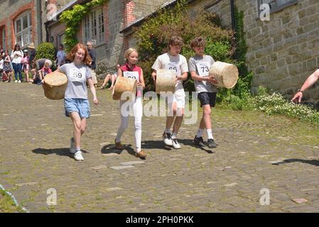 Vier Kinder tragen ihre „Käsesorten“ während des Food and Drink Festivals der Stadt bis zur Startlinie des Käserennens auf dem Gold Hill, Shaftesbury. Stockfoto
