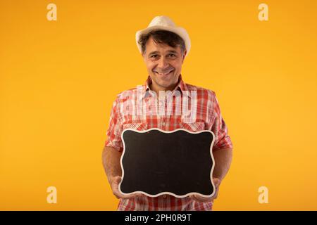 Schwarzhaariger Mann mit Hut und farbenfrohem Hemd, lächelnd, mit einem Black-Board-Schild in den Händen Stockfoto