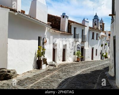 Alte kopfsteingepflasterte Gasse mit traditionellen weißen Häusern in Monsaraz, von Mauern umgebenes mittelalterliches Dorf in der portugiesischen Region Alentejo nahe der Grenze zu Spanien Stockfoto