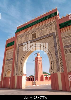 Rissani-Tor - Bab Rissani an einem sonnigen Morgen mit dem Minarett einer Moschee, das durch den zentralen Bogen gesehen wird Stockfoto