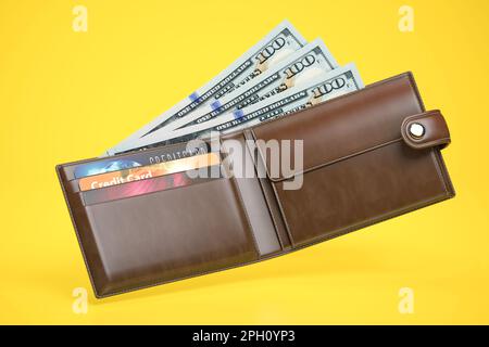 Öffnen Sie die Lederbörse mit Dollars und Kreditkarten auf gelbem Hintergrund. 3D Abbildung Stockfoto