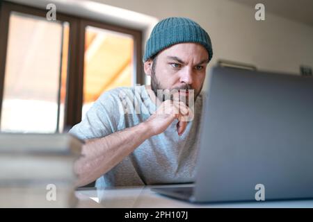 Junger moderner Unternehmer, der zu Hause an seinem Laptop arbeitet. Stockfoto