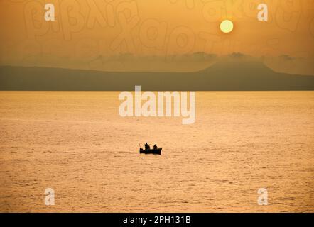 Rethymnon Sonnenuntergang mit Fischern in einem kleinen Boot, der Himmel hat einige griechische Schriftzeichen Stockfoto