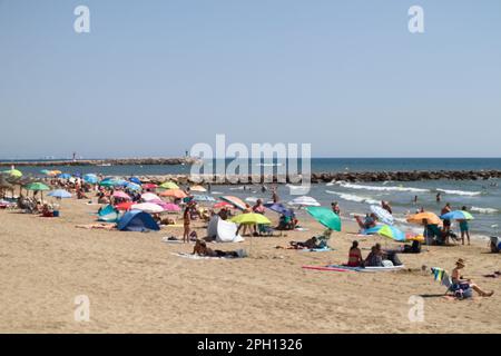 Verschwommenes Bild einer Landschaft mit einem Strand voller Leute, die mit ihren Sonnenschirmen und Handtüchern sonnen. Speicherplatz kopieren Stockfoto