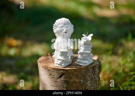 Die kleine Igelstatue neben dem Bücherstapel befindet sich auf einem Holzstumpf auf grünem Hintergrund, süße Kinder machen Igelfiguren über Lernen und Bücher readi Stockfoto