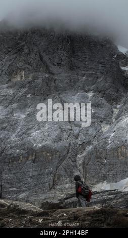 Ein Mann, der einen Rucksack trägt, während er vor einem Hintergrund schneebedeckter Gipfel steht Stockfoto