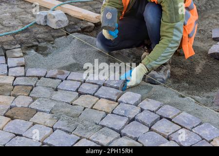 Arbeiter legten sorgfältig Granitsteine und benutzten industrielle Kopfsteinpflaster, um langlebigen und langlebigen Bürgersteig zu schaffen. Stockfoto