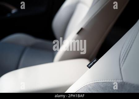 Flacher Fokus eines SRS-Airbag-Tags, das in einem Hybrid-Fahrzeug mit neuer Technologie an den Vordersitzen in Leder angebracht ist. Die mittlere Armlehne ist ebenfalls zu sehen Stockfoto