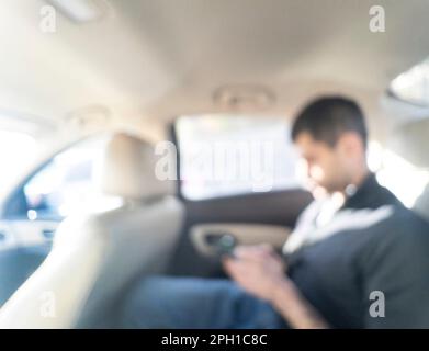 Abstrakter, unscharfer Hintergrund mit man Touch Mobiltelefon und Sitz im Auto. Verschwommenes Fahrzeug mit Person Stockfoto
