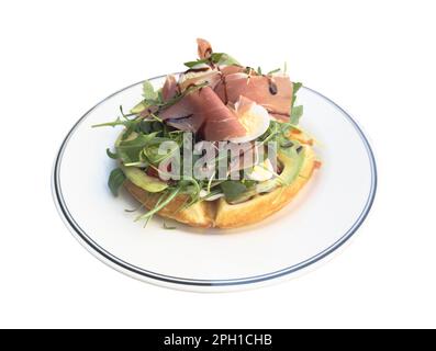 Frühstückszeit. Waffeln mit Prosciutto, Salat und Ei zum Frühstück isoliert auf weißem Hintergrund. Stockfoto