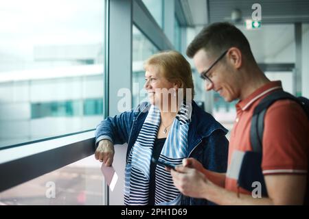 Passagiere warten am Flughafen. Glückliche Seniorin mit ihrem erwachsenen Sohn vor dem Einsteigen in das Flugzeug. Stockfoto