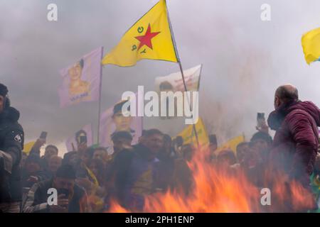 25. März 2023, Hessen, Frankfurt/Main: Teilnehmer stehen mit Flaggen vor einem Feuer. Bei der zentralen Feier des kurdischen Neujahrs „Newroz“. In der Mitte ist eine Flagge der YPG, einer bewaffneten kurdischen Miliz. Tausende von Menschen aus ganz Deutschland haben sich im Rebstockpark versammelt, um das kurdische Neujahr „Newroz“ zu feiern. Foto: Andreas Arnold/dpa Stockfoto