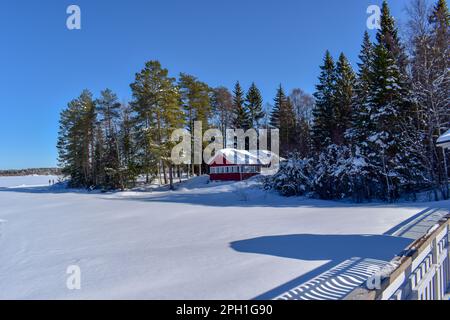 Wunderschöne superfinnische Winterlandschaft mit rotem finnischem Holzhaus im Winter mit Schnee bedeckt. März 2023 Stockfoto