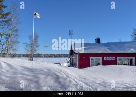 Wunderschöne superfinnische Winterlandschaft mit rotem finnischem Holzhaus im Winter mit Schnee bedeckt. März 2023 Stockfoto