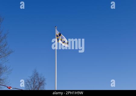 Finnische Nationalflagge auf einem Fahnenmast vor dem blauen Himmel. Finlandssvensk Stockfoto