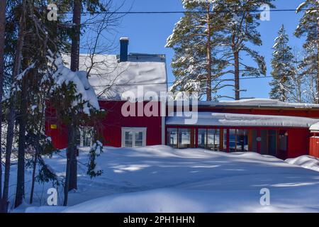 Wunderschöne superfinnische Winterlandschaft mit rotem finnischem Holzhaus im Winter mit Schnee bedeckt. März 2023 Stockfoto