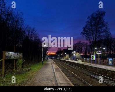 Northern Rail Klasse 150 DMU Zug, Ankunft am kleinen 2 Bahnsteig Chapel-en-Le-Frith Bahnhof, Derbyshire in der Dämmerung mit einem roten Sonnenuntergang Stockfoto