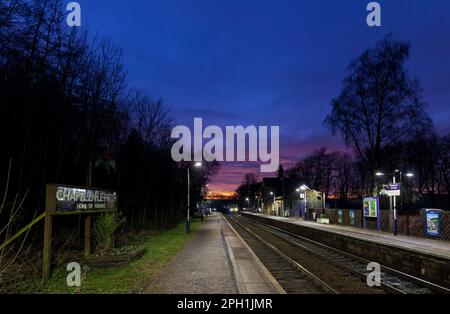 Northern Rail Klasse 150 DMU Zug, Ankunft am kleinen 2 Bahnsteig Chapel-en-Le-Frith Bahnhof, Derbyshire in der Dämmerung mit einem roten Sonnenuntergang Stockfoto