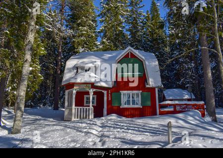 Wunderschöne superfinnische Winterlandschaft mit rotem finnischem Holzhaus im Winter mit Schnee bedeckt. März 2023 Stockfoto
