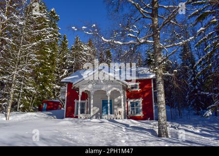 Wunderschöne superfinnische Winterlandschaft mit rotem finnischem Holzhaus im Winter mit Schnee bedeckt. März 2023 Stockfoto