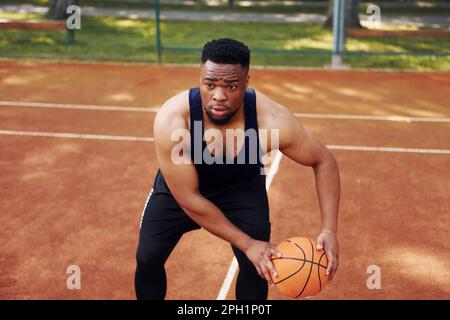 Ein afroamerikanischer Mann spielt Basketball auf dem Platz im Freien Stockfoto