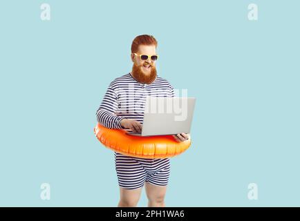 Lustiger Mann in Erwartung des Sommerurlaubs mit Laptop-Buchung auf hellblauem Hintergrund. Stockfoto