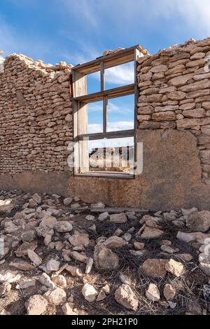 Zerbröckelnde Hauswand aus ordentlich gestapelten weißen Felsen in einer Geisterstadt in Yeso, New Mexico. Ein BNSF-Güterzug ist durch das Fenster zu sehen. Stockfoto