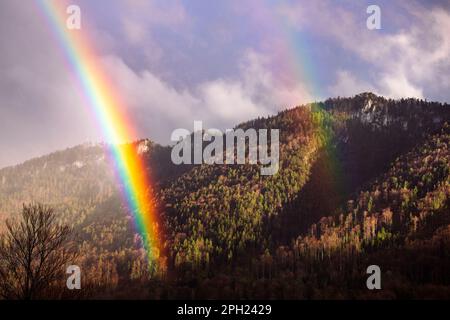 Regenbogen in den Jura Mountains. Landschaftlich reizvolle Landschaft mit dulierendem Regenbogen und Blick auf die Berge, Frühlingswetter. Schweizer Jura. Stockfoto