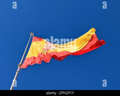 Spanische Nationalflagge auf blauem Himmelshintergrund. Die Fahne am Fahnenmast flattert im Wind. Spanische Flagge bläst im Wind gegen klares Blau Stockfoto