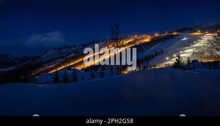 Nachtsicht über das Skigebiet in Lichtern und majestätischen schneebedeckten Bergen am Winterabend. Stockfoto