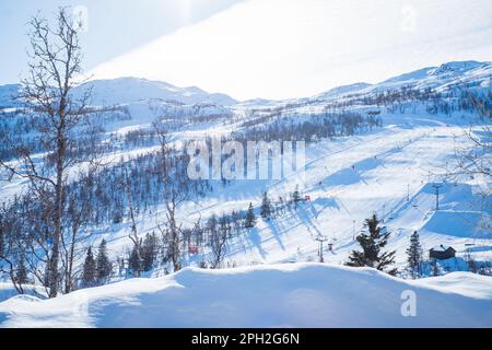 Blick auf das Skigebiet mit Pisten, Sesselliften und majestätischen schneebedeckten Bergen am Wintertag. Stockfoto