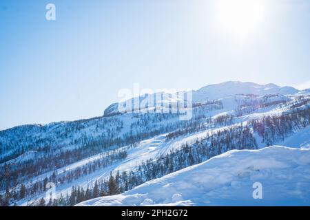 Blick auf das Skigebiet mit Pisten, Sesselliften und majestätischen schneebedeckten Bergen am Wintertag. Stockfoto