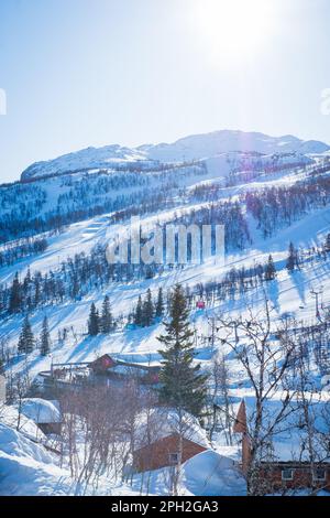 Blick auf das Skigebiet mit Pisten, Sesselliften und majestätischen schneebedeckten Bergen am Wintertag. Stockfoto