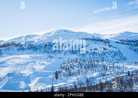 Blick auf das Skigebiet mit Pisten, Sesselliften und majestätischen schneebedeckten Bergen am Wintertag. Stockfoto