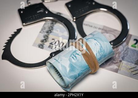 Handschellen liegen auf dem Tisch neben einem Bündel brasilianisches Geld, Konzept, kriminelle Aktivitäten in Brasilien, illegale Geschäfte, Schwarzmarkt Stockfoto