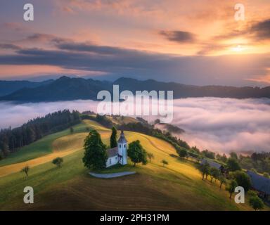 Luftaufnahme der kleinen Kirche auf dem Hügel über rosa niedrige Wolken Stockfoto