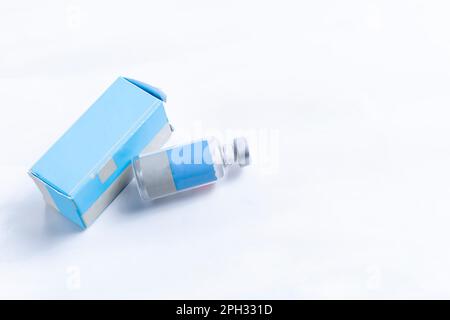 Medizinische Glasflasche mit blauem Kasten auf weißem Hintergrund. Selektiver Fokus. Stockfoto