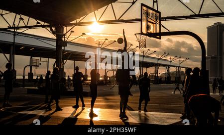 Leute, die bei Sonnenuntergang draußen Basketball spielen Stockfoto