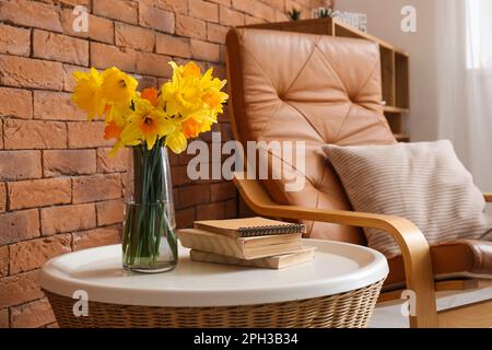 Vase mit Narzissen, Blumen und Büchern auf dem Couchtisch neben dem Sessel im Wohnzimmer Stockfoto