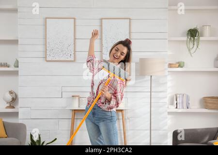 Frau mit Mopp, die beim Putzen zu Hause singt Stockfoto